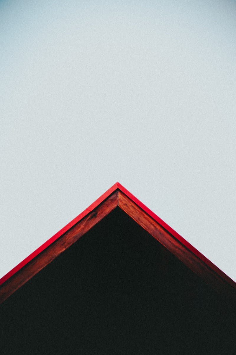 Artistic view of a red roof peak contrasting with a clear blue sky.