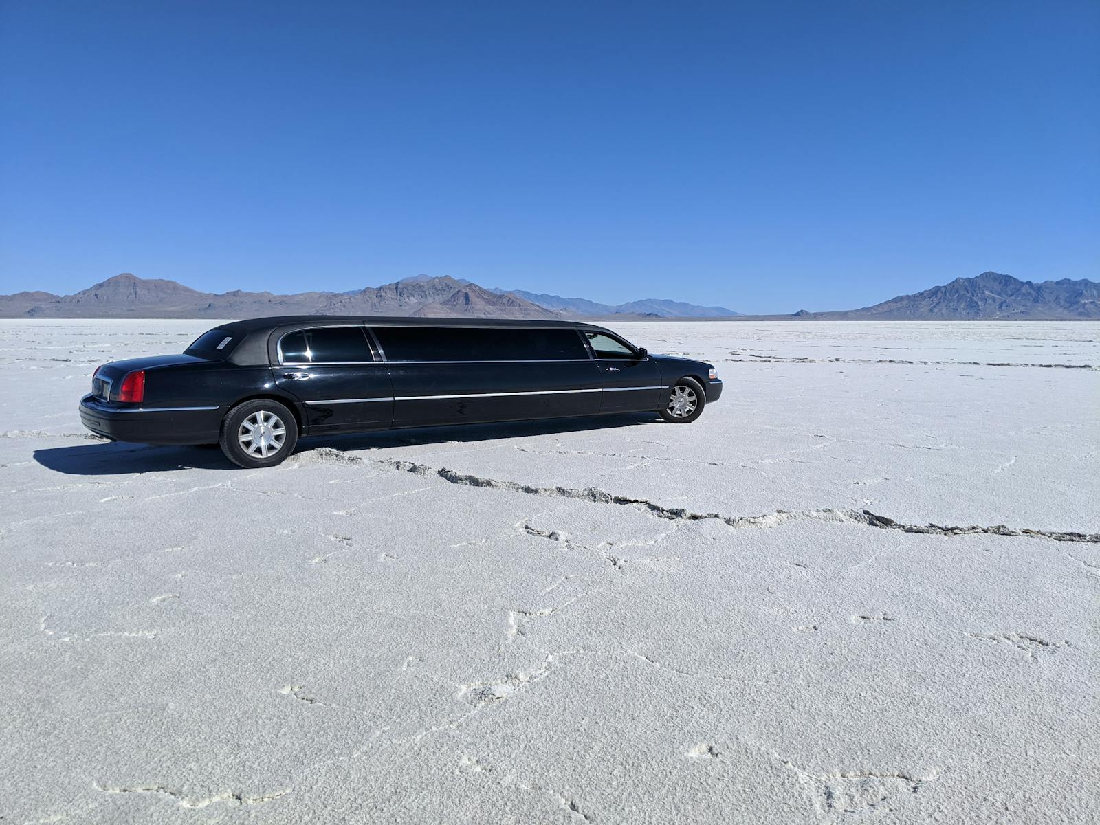 A sleek black limousine parked in a vast, dry desert with a clear blue sky.